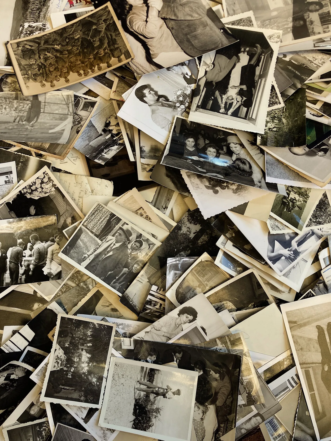 A large pile of scattered black and white vintage photographs, showing people, group gatherings, outdoor scenes, and various moments from past decades. | En-dash.co.uk